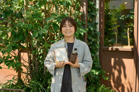 緑に囲まれた店先でLOVEGのソイミールとソースを手に持つ人